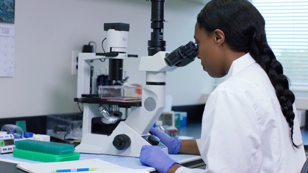female scientist at Nutramax Laboratories examining a slide through a microscope